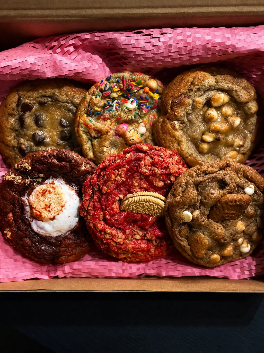 Pink-lined gift box filled with six gourmet cookies including chocolate chip, birthday cake, white chocolate macadamia, red velvet s'mores, strawberry crunch and pecan
